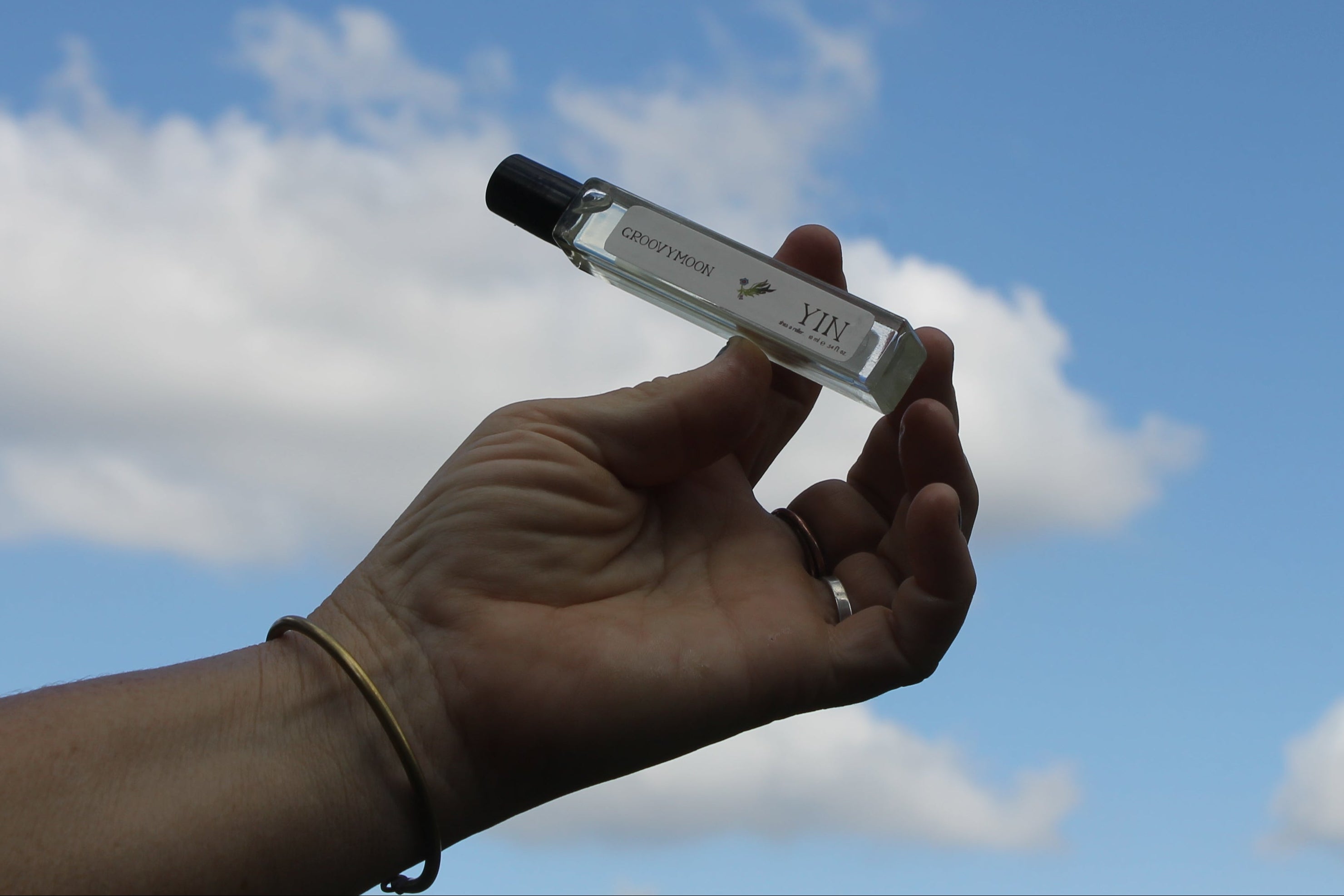 Hand holding a small perfume roller against a blue sky with clouds